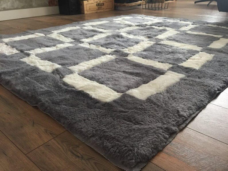 May include: A grey and white sheepskin rug with a geometric pattern. The rug has a soft, fluffy texture.