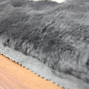 May include: Close-up of a grey faux fur rug with a dark grey backing. The rug has a soft, plush texture and is perfect for adding warmth and comfort to any room.