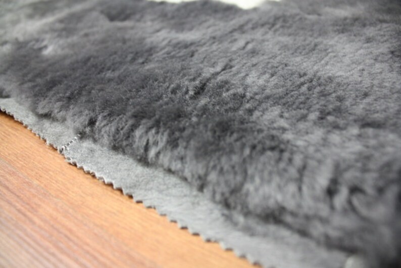 May include: Close-up of a grey faux fur rug with a dark grey backing. The rug has a soft, plush texture and is perfect for adding warmth and comfort to any room.