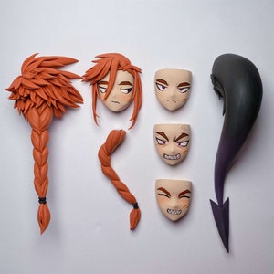 Könnte beinhalten: Fünf verschiedene Tonfiguren, darunter vier Gesichter mit unterschiedlichen Ausdrücken und ein langes, geflochtenes Haarstück. Die Gesichter sind alle hellhäutig mit bemalten Gesichtszügen, einschließlich Augen, Augenbrauen und Mund. Das Haarstück ist leuchtend orange.