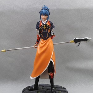 May include: A blue-haired figurine of a woman wearing a black and orange outfit with a spear. She is standing on a stone base.