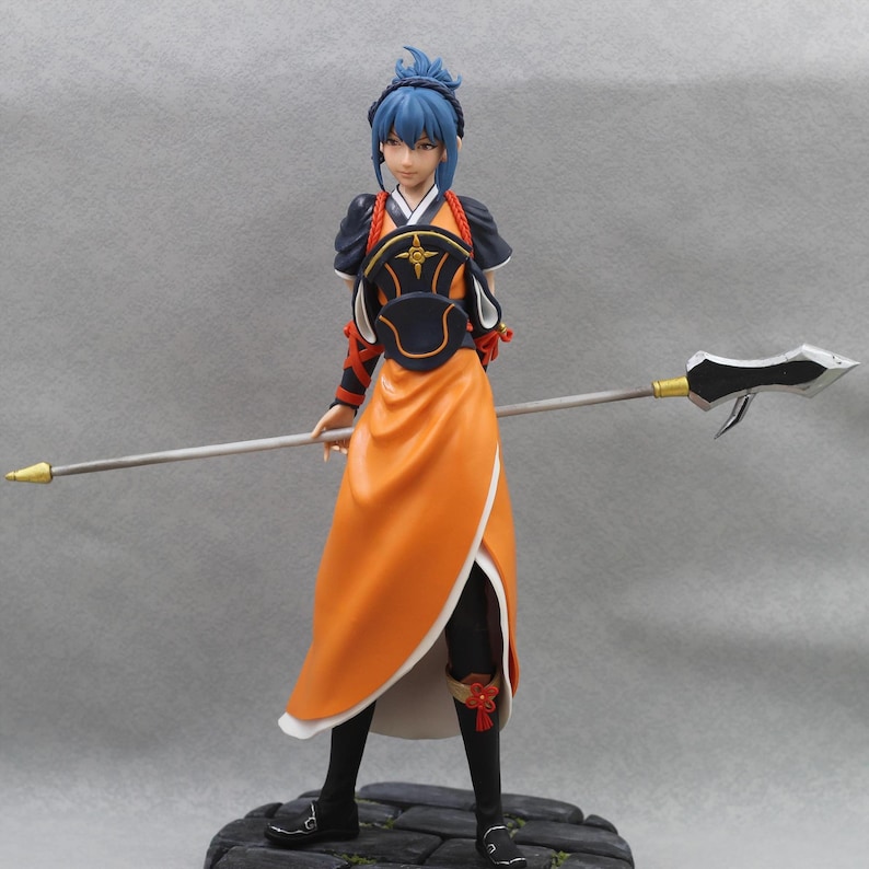 May include: A blue-haired figurine of a woman wearing a black and orange outfit with a spear. She is standing on a stone base.