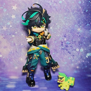 May include: A detailed figurine of a character with black hair, teal accents, and a teal and black outfit. The figure is posed with one hand up and a peace sign. A pixelated green and yellow creature is at the figure's feet.
