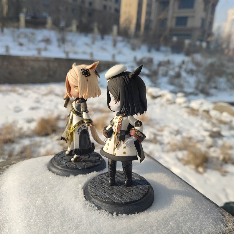 K&ouml;nnte beinhalten: Zwei kleine, detaillierte Figuren von Anime-Charakteren. Die Figur links ist eine weibliche Figur mit blonden Haaren, die ein wei&szlig;es und schwarzes Kleid mit goldenen Akzenten tr&auml;gt. Die Figur rechts ist eine weibliche Figur mit schwarzen Haaren, die eine wei&szlig;e und schwarze Milit&auml;runiform mit goldenen Akzenten tr&auml;gt. Beide Figuren stehen auf schwarzen runden Sockeln.