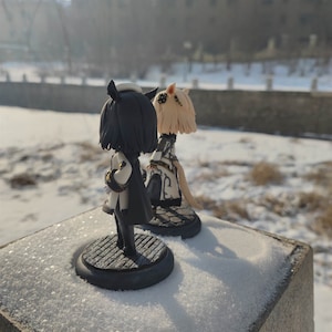 K&ouml;nnte beinhalten: Zwei kleine, handbemalte Figuren von Anime-Charakteren. Die Figur links tr&auml;gt ein schwarz-wei&szlig;es Outfit und hat schwarze Haare. Die Figur rechts tr&auml;gt ein wei&szlig;-schwarzes Outfit und hat blonde Haare. Beide Figuren stehen auf einem grauen Sockel.