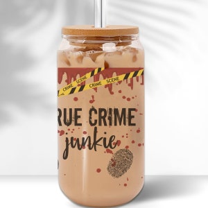 May include: A clear glass tumbler with a bamboo lid and a straw. The tumbler is filled with a light brown liquid and has a red and yellow crime scene tape design with the text "TRUE CRIME junkie".