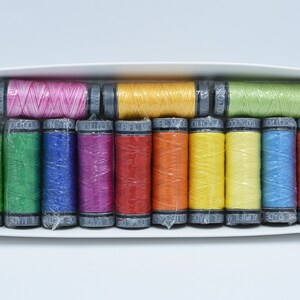 May include: A collection of colourful sewing thread spools presented in a white box. The spools are encased in transparent plastic and display a spectrum of hues, such as pink, yellow, green, blue, and orange. The spools are neatly arranged within the box.