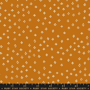 May include: Mustard-coloured fabric featuring a repeating pattern of small, white floral shapes. The fabric has a textured appearance and a ruler is at the bottom. The text "RUBY STAR SOCIETY" is printed on the ruler.