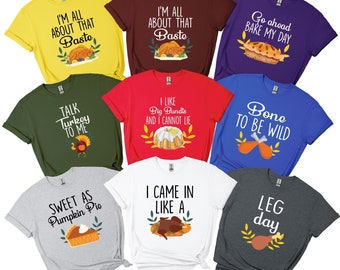 May include: A collection of colorful t-shirts with Thanksgiving-themed graphics and text. The shirts feature phrases like "I'm all about that baste," "Talk turkey to me," and "Sweet as pumpkin pie." Each shirt has a unique design.