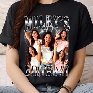 Puede incluir: Camiseta negra con un gr&aacute;fico plateado estilizado que dice "MILEY'S 23rd BIRTHDAY". El dise&ntilde;o incorpora m&uacute;ltiples im&aacute;genes de una mujer, cada una mostrando diferentes gestos con las manos y expresiones faciales, con acentos de rayos.