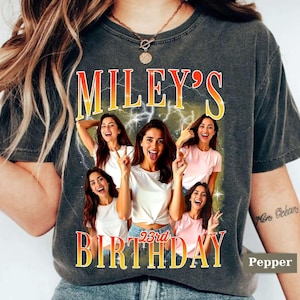 Puede incluir: Camiseta gris oscuro con un gr&aacute;fico que muestra el texto "MILEY'S 23rd BIRTHDAY" en una fuente degradada amarilla y naranja. El gr&aacute;fico incluye m&uacute;ltiples im&aacute;genes de una mujer en varias poses. La palabra "Pepper" est&aacute; en la esquina inferior derecha.