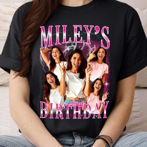 Puede incluir: Camiseta negra con un dise&ntilde;o que dice "MILEY'S 23rd BIRTHDAY". El dise&ntilde;o muestra a una mujer haciendo el signo de la paz y sacando la lengua, sobre un fondo de rayos rosas y morados.