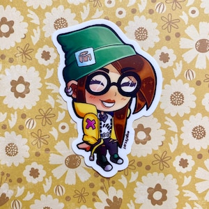 Könnte beinhalten: Ein Cartoon-Aufkleber eines jungen Menschen, der eine grüne Mütze, eine gelbe Jacke und eine schwarze Hose trägt. Die Person hat braunes Haar, braune Augen und trägt eine Brille. Der Aufkleber hat einen weißen Hintergrund und befindet sich auf einem gelben Blumenhintergrund.