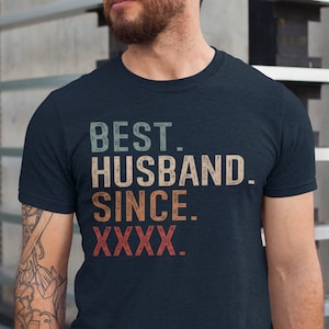 May include: A navy blue t-shirt with a vintage-style graphic that reads "BEST. HUSBAND. SINCE. XXXX."