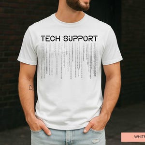 K&ouml;nnte beinhalten: Wei&szlig;es T-Shirt mit dem schwarzen Aufdruck "TECH SUPPORT" auf der Brust. Darunter befindet sich eine Grafik aus vertikalen Linien, die an Bin&auml;rcode erinnern. Das kurz&auml;rmelige Shirt ist aus weichem Material.