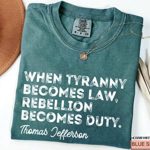 May include: A teal blue t-shirt with a white distressed graphic that reads "When tyranny becomes law, rebellion becomes duty. Thomas Jefferson".