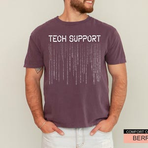 K&ouml;nnte beinhalten: Beerenfarbenes T-Shirt mit den Worten "TECH SUPPORT" in wei&szlig;en Blockbuchstaben &uuml;ber einem vertikalen Bin&auml;rcode-Design. Das Shirt ist von der Marke Comfort Colors.