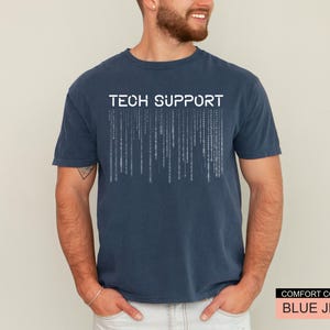 K&ouml;nnte beinhalten: Ein marineblaues T-Shirt mit den wei&szlig;en Worten "TECH SUPPORT" &uuml;ber einer Matrix-Grafik. Das Shirt ist von der Marke Comfort Colors in der Farbe "Blue Jean".