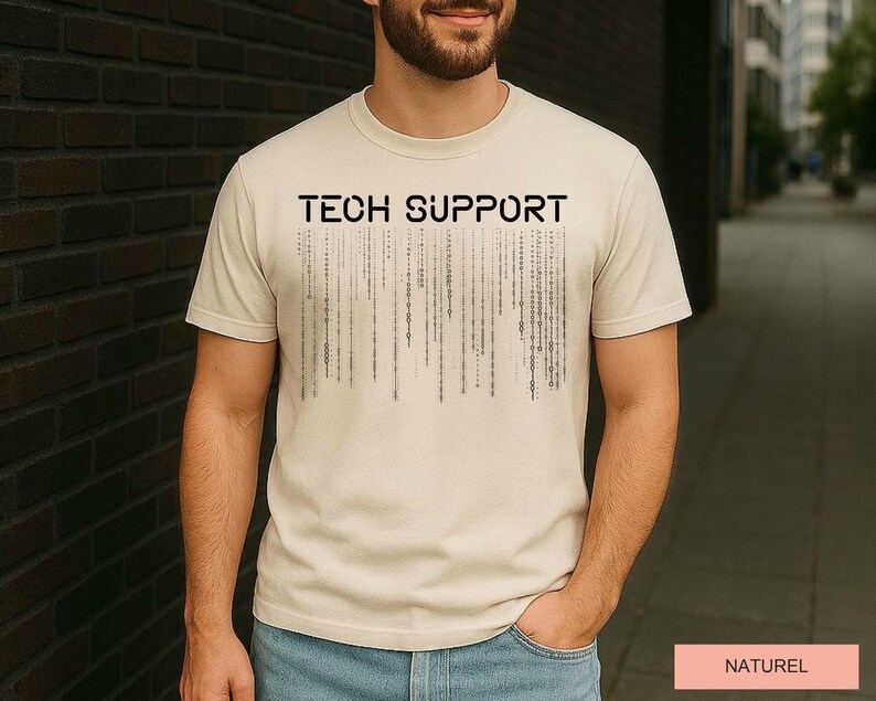 K&ouml;nnte beinhalten: Beiges T-Shirt mit dem schwarzen Aufdruck "TECH SUPPORT" auf der Brust. Darunter befindet sich eine Grafik aus vertikalen Linien, die an Bin&auml;rcode erinnern. Das Wort "NATUREL" ist auf einem rosa Rechteck gedruckt.