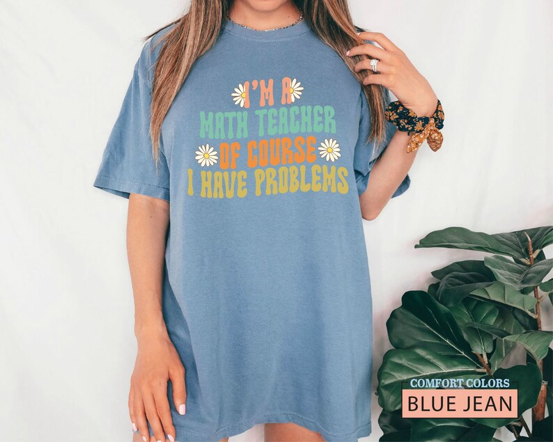 Pode incluir: Uma camiseta azul jeans com o texto "I'm a math teacher of course I have problems" em uma fonte retr&ocirc; com detalhes de margaridas.