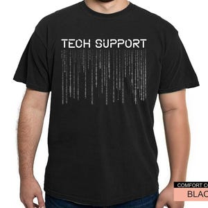 K&ouml;nnte beinhalten: Schwarzes T-Shirt mit dem wei&szlig;en Text "TECH SUPPORT" &uuml;ber einer vertikalen Grafik im Matrix-Stil. Das T-Shirt hat einen Rundhalsausschnitt und scheint aus einem weichen Material zu sein. Das T-Shirt ist eine Komfortfarbe.