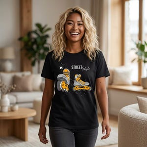 Puede incluir: Una camiseta negra de manga corta con un estampado gráfico de dos patines en línea en tonos naranja, gris y blanco. El texto "STREET Style" está impreso en blanco sobre los patines, acompañado de pequeños detalles de salpicaduras blancas.