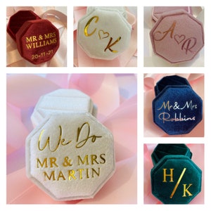 May include: A collection of octagonal velvet ring boxes in various colors including deep red, white, dusty pink, navy blue, and emerald green. Each box features gold or rose gold foil lettering with personalized names, dates, or initials.