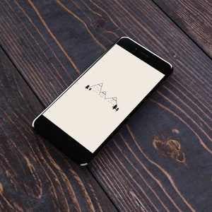 May include: A black smartphone with a white screen displaying a simple line drawing of mountains and trees. The phone is lying on a dark wood surface.