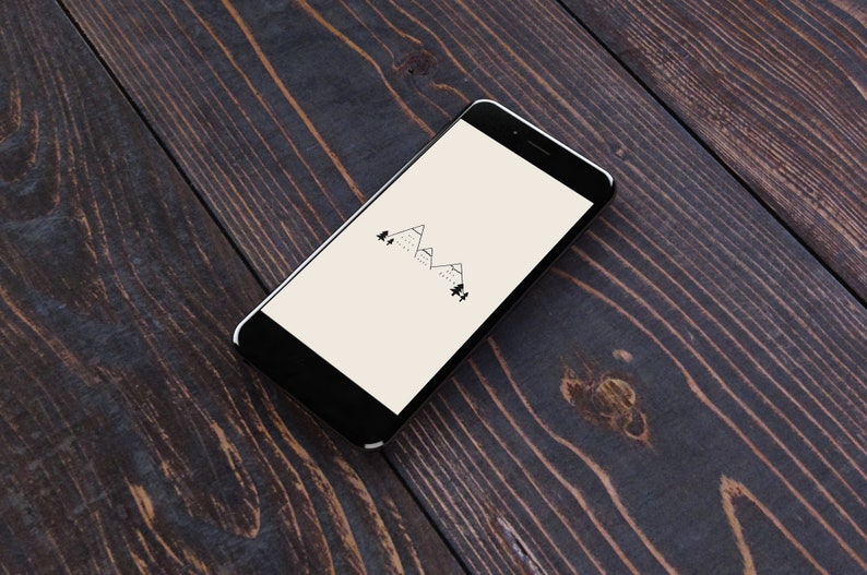 May include: A black smartphone with a white screen displaying a simple line drawing of mountains and trees. The phone is lying on a dark wood surface.