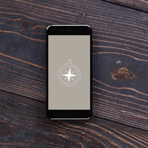 May include: A black smartphone with a compass icon on the screen. The phone is lying on a dark wood surface.