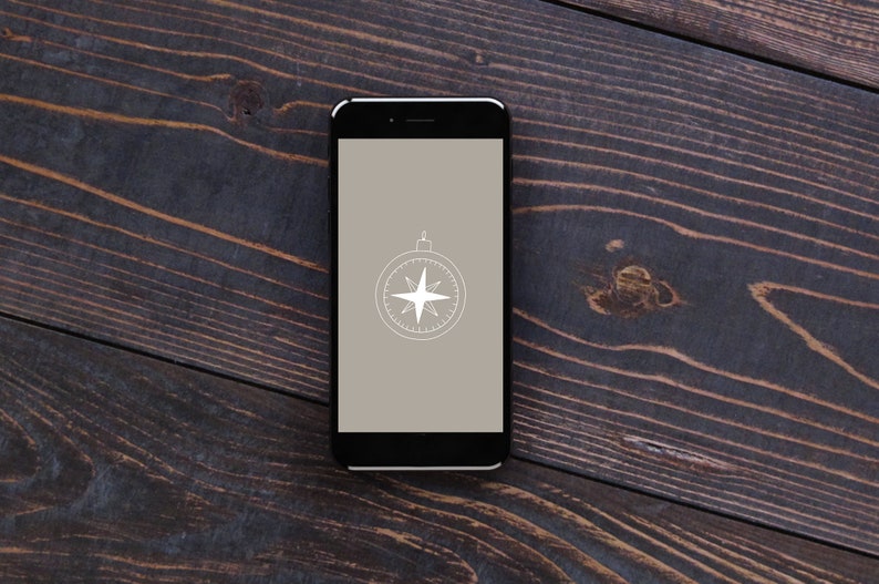May include: A black smartphone with a compass icon on the screen. The phone is lying on a dark wood surface.