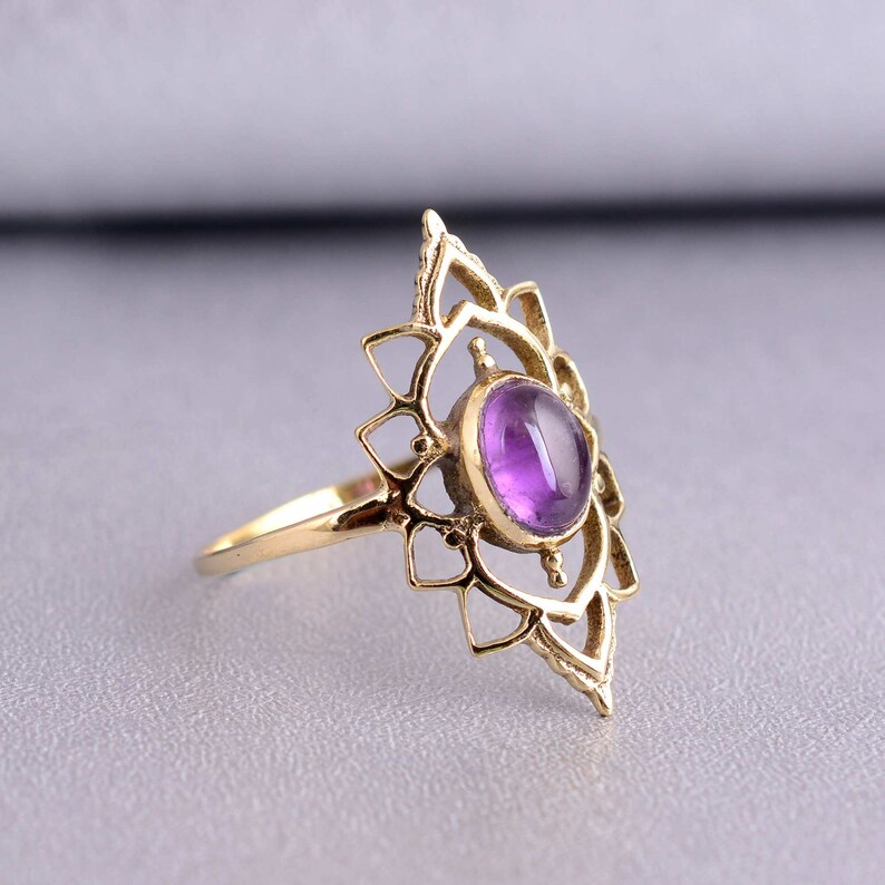 May include: A gold ring with a delicate, intricate design featuring a purple amethyst gemstone in the center.