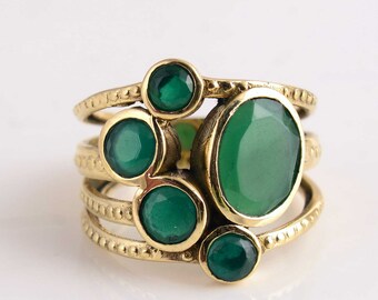 Può includere: Un anello d'oro con più bande e cinque pietre preziose verdi. La pietra preziosa più grande è di forma ovale e le altre quattro sono rotonde.