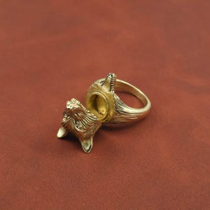 May include: A gold-colored ring featuring a detailed wolf design. The ring's head opens to reveal a hollow interior. The wolf's fur and facial features are intricately carved, creating a unique and artistic piece of jewelry.