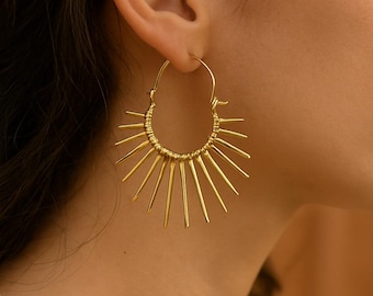 May include: Gold hoop earrings with a sunburst design. The earrings are made of thin metal wires that radiate out from the hoop.
