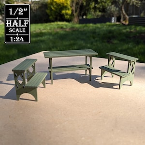 May include: A miniature sage green wooden table and two matching benches with a lattice side design. The set is labeled 1/2 inch half scale 1:24. The table features a slatted top and a lower shelf, while the benches have a two-tier step design.