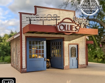 May include: A model kit of a vintage motor garage with a red roof and white siding. The garage has a sign that reads "Ollie's Motor Garage". The kit is 1:48 scale and is made by Pacific Northwest Miniatures.