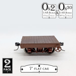 May include: A brown model flat car with a wooden deck, metal wheels, and a handbrake. The text "7' FLAT CAR" is below the model. The image also includes text that reads "1:48 SCALE" and "2' NARROW GAUGE".