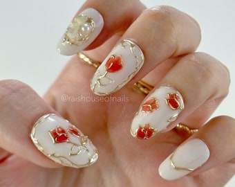 Uñas postizas con diseño de rosa roja, contornos cromados dorados y detalle de gema de ópalo.