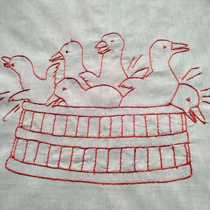 Puede incluir: Diseño bordado en rojo de cinco pájaros en un cubo de madera. Los pájaros están todos mirando en diferentes direcciones y tienen características simples y estilizadas.
