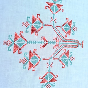 以下が含まれることがあります： 赤と緑の刺繍が施された白いリネン製のテーブルクロス。デザインは、枝と葉を持つスタイリッシュな木を特徴としています。