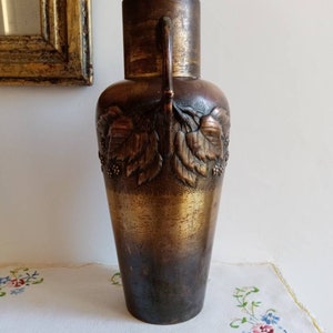 Op de afbeelding: Een hoge, antieke bronzen vaas met een getextureerd oppervlak en reli&euml;fmotieven van bladeren. De vaas heeft twee handvatten en een licht uitlopende opening.