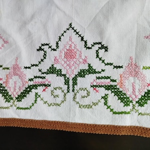 May include: White linen tablecloth with a brown crocheted border and embroidered floral design in pink and green.
