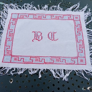 May include: White linen napkin with a red and blue embroidered border and the initials "B C" in the centre.