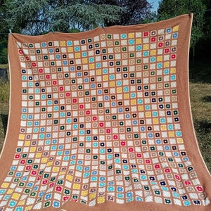 May include: A large brown crocheted blanket with a pattern of colorful squares. The blanket is made with a variety of colors, including red, blue, green, yellow, and white.