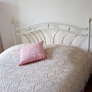 May include: A white metal bed frame with a gold-coloured headboard and a white crocheted bedspread. A pink pillow with a floral pattern is on the bed.