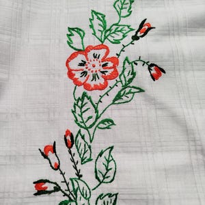 Peut inclure: Tissu blanc avec un motif floral brodé en vert et rouge. Le motif présente une grande fleur rouge avec un centre noir et des feuilles vertes.
