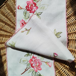 Peut inclure: Deux chemins de table en lin blanc avec des motifs floraux brodés en rose. Les chemins de table ont un bord festonné rose.