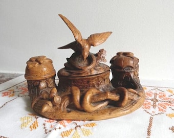 May include: A carved wooden decorative piece featuring a bird perched atop a central container, flanked by two smaller containers. The piece is intricately carved with a natural wood finish, showcasing detailed craftsmanship and a rustic aesthetic.