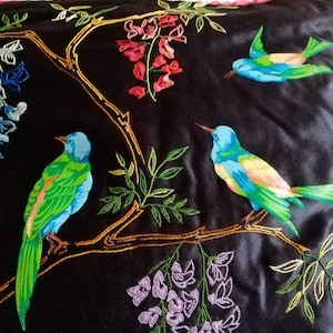 Puede incluir: Almohada de terciopelo negro con pájaros y flores bordadas. Los pájaros son verdes, azules y amarillos. Las flores son moradas, rojas y rosas.
